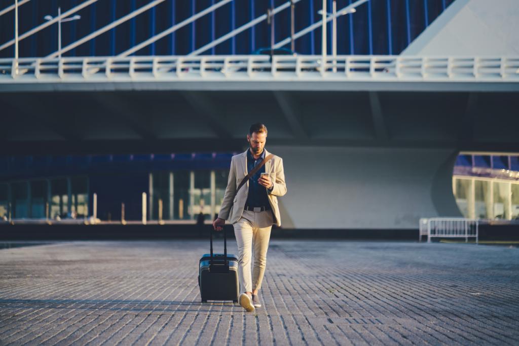 Man walking outside of airport checking his phone carrying luggage